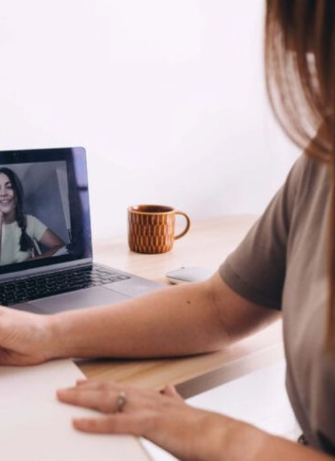 Person participating in a video call on a laptop, with a woman smiling on the screen and a coffee mug in the background.